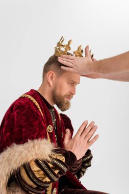 cropped view of man putting crown on king with praying hands on grey background 