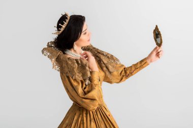 side view of queen with crown looking at mirror isolated on grey