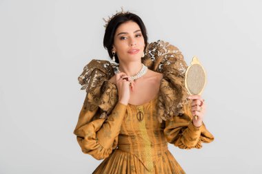 queen with crown holding mirror and looking at camera isolated on grey