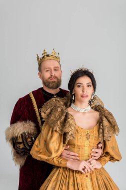 king with crown hugging attractive queen isolated on grey