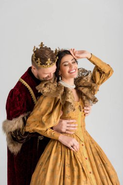 king with crown hugging smiling queen isolated on grey