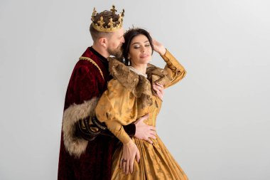 king with crown kissing and hugging smiling queen isolated on grey