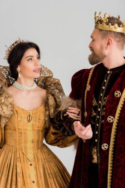 queen and smiling king with crowns holding hands isolated on grey