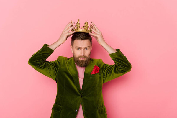 man in velour jacket wearing crown on pink background  