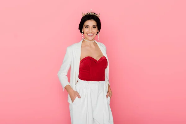 smiling woman with crown looking at camera isolated on pink