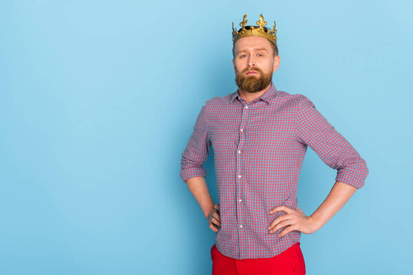 serious man with crown with hands on hips looking at camera on blue background 