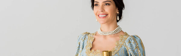 panoramic shot of smiling queen holding cup isolated on grey