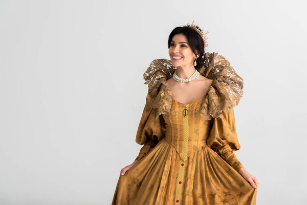 smiling queen with crown looking away isolated on grey