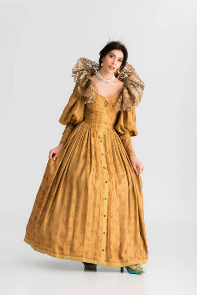 привлекательная королева с короной, смотрящая на камеру на сером фоне
 