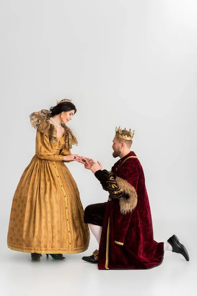 smiling queen and king with crowns holding hands on grey background