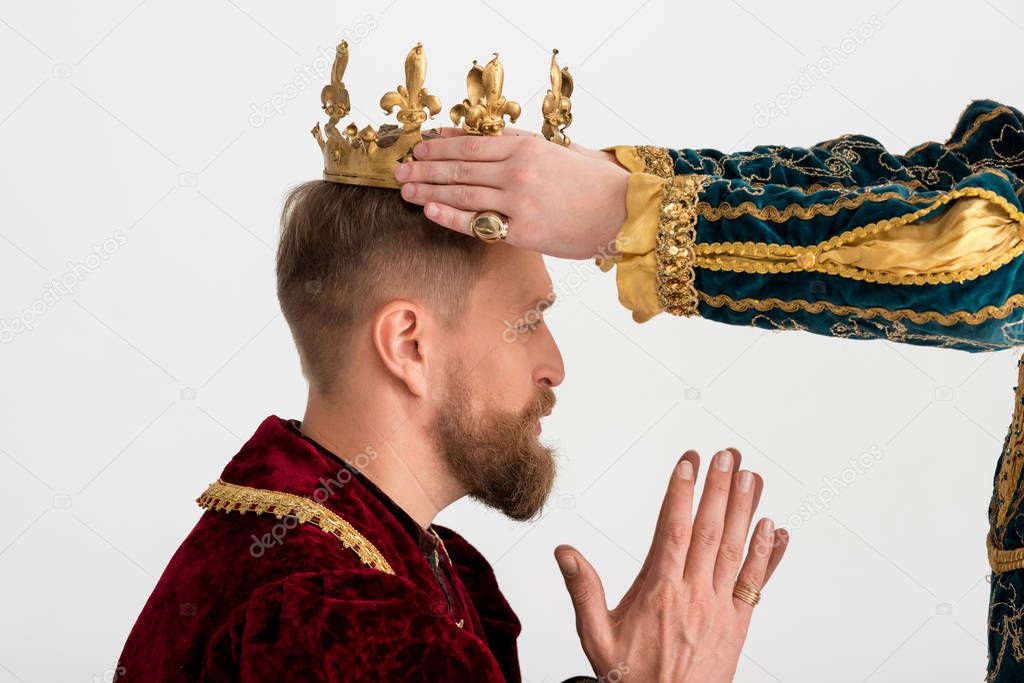 cropped view of man putting crown on king with praying hands on grey background 