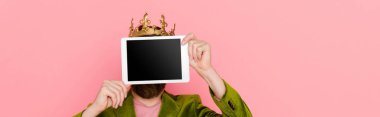 panoramic shot of man with crown holding digital tablet isolated on pink 