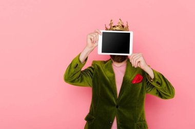 man with crown holding digital tablet with copy space isolated on pink 