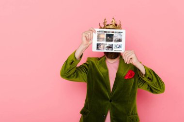 KYIV, UKRAINE - DECEMBER 3, 2019: man with crown holding digital tablet with pinterest app isolated on pink