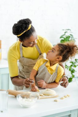 Mutlu Afro-Amerikan annesi tapılası çocuğa bakıyor ve mutfakta hamur köftesi yapıyor. 