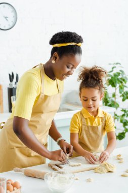 Neşeli Afro-Amerikan anne ve kızı kesme tahtasında hamur işi yapıyorlar. 