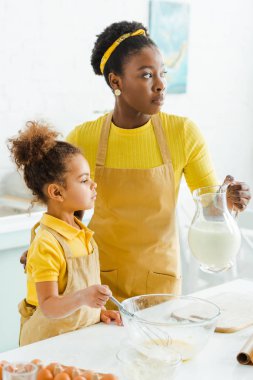 Çekici Afrikalı Amerikalı anne, tatlı kızının yanında sütle sürahi tutuyor. 