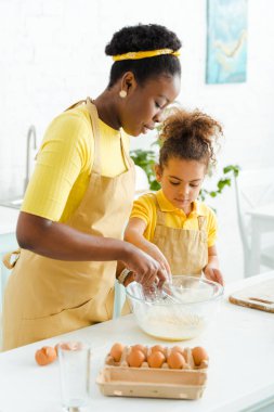 Çekici Afro-Amerikan annesi kase ve kızının yanında çırpı tutuyor. 