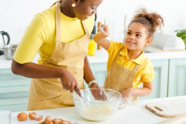 Sevimli Afrikalı Amerikalı çocuk mutfaktaki mutlu anneyi işaret ediyor. 