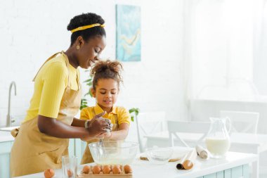 Sevimli Afrikalı Amerikalı çocuk ve neşeli anne mutfakta yemek pişirirken gülümsüyor. 