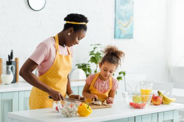 Afro-Amerikan anne ve kızı mantar keserken bıçak tutuyorlar. 