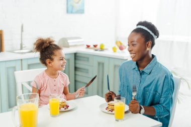 Neşeli Afro-Amerikan anne ve kızı lezzetli kreplerin yanında çatal bıçak takımı tutuyor. 