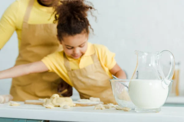 ボウルの近くに牛乳とかわいいアフリカ系アメリカ人の子供が母親の近くに餃子をすくい取るという選択的な焦点 — ストック写真