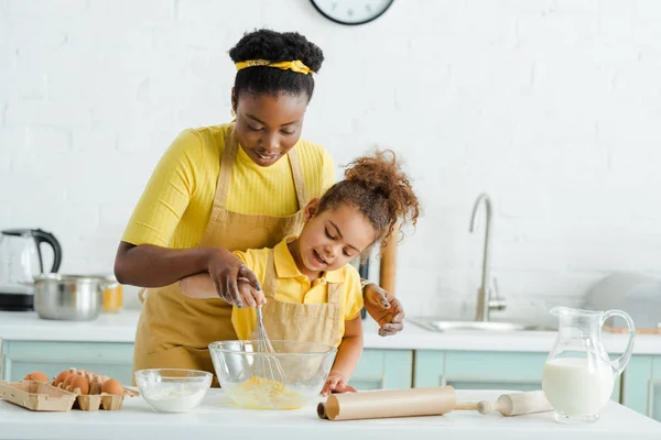 かわいいアフリカ系アメリカ人の子供は台所で陽気な母親の近くのボウルを見て — ストック写真