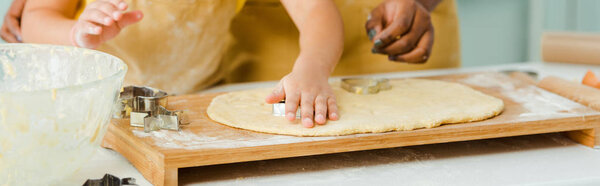 панорамный снимок африканской матери и дочери, держащих кусачки для печенья рядом с тестом
 