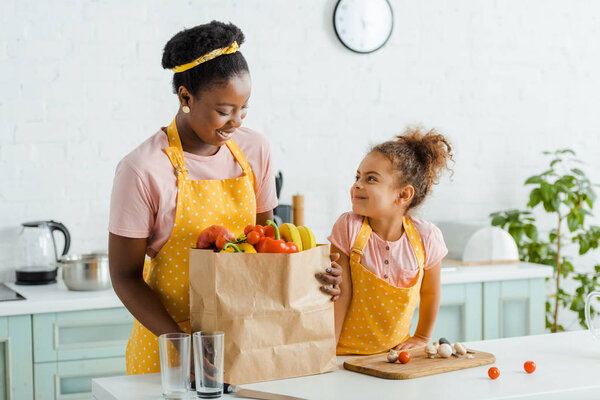 happy african american kid looking at mother near groceries 