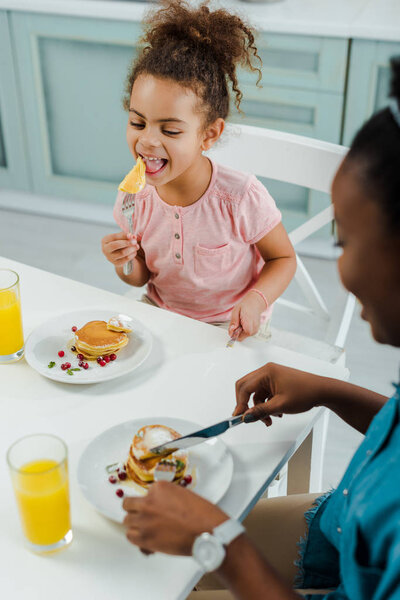 selective focus of happy african american kid eating pancakes near mother 