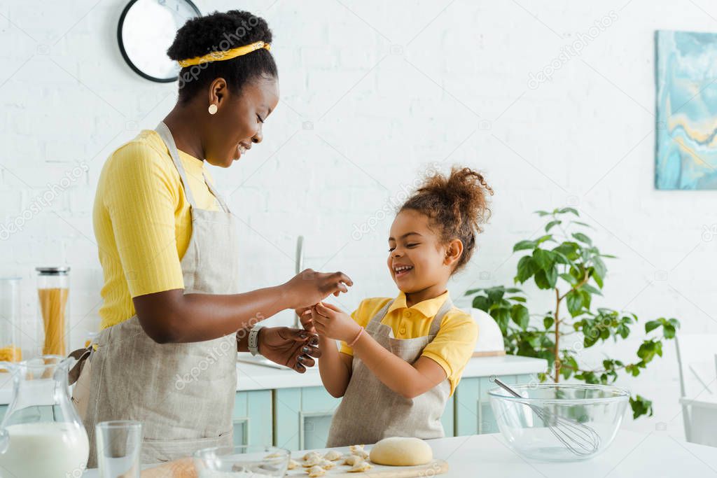 happy african american mother and daughter sculpting raw dough while cooking dumplings 