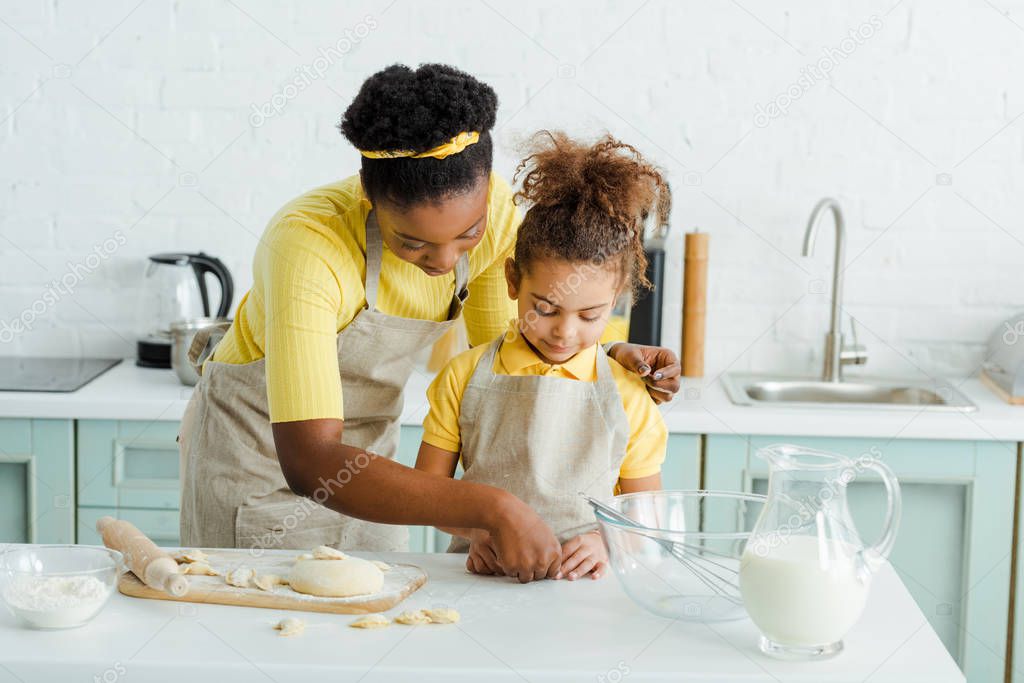 african american mother near adorable daughter sculpting dumplings in kitchen 