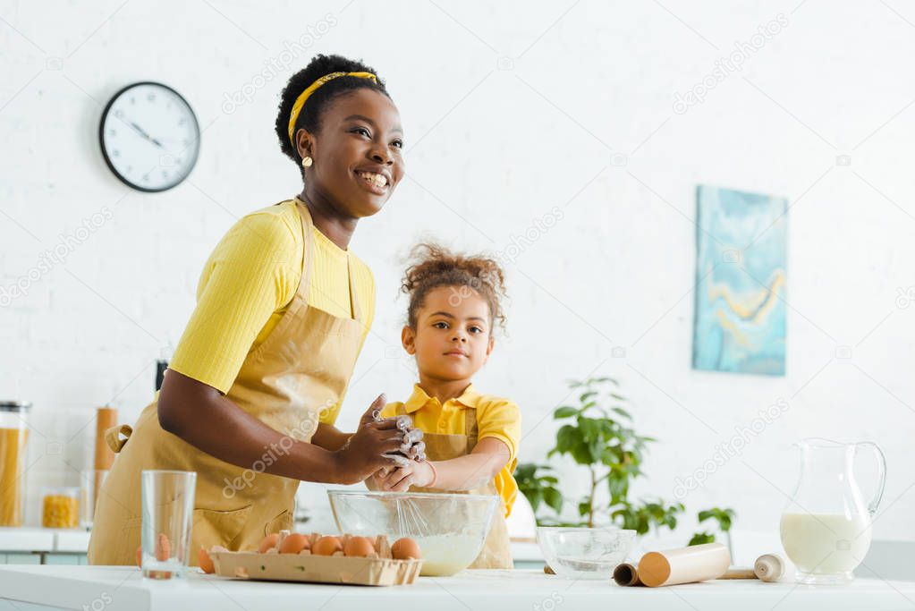 african american kid and cheerful mother smiling while cooking in kitchen 