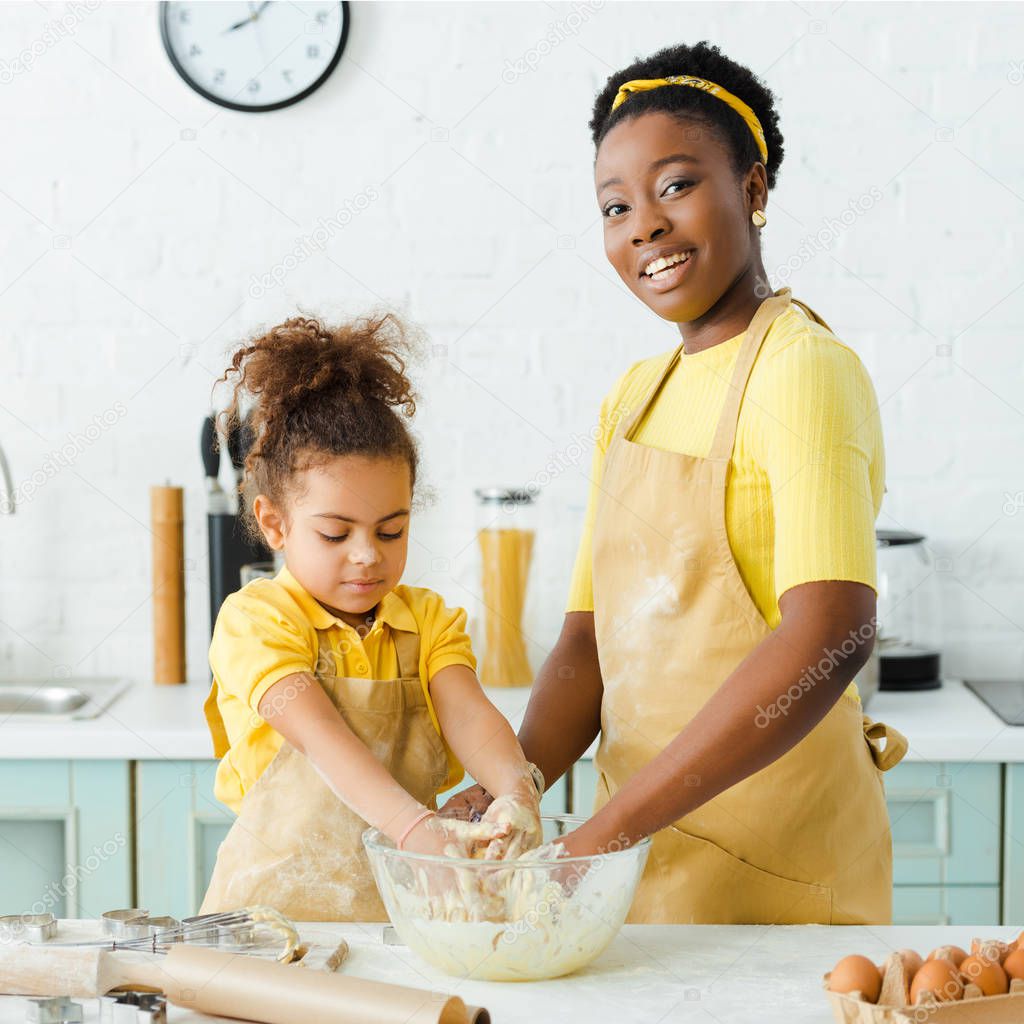 happy african american mother and daughter kneading dough 