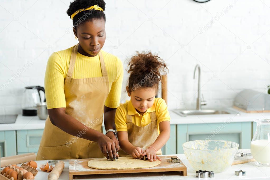 adorable african american kid and mother holding cookie cutters near raw dough 