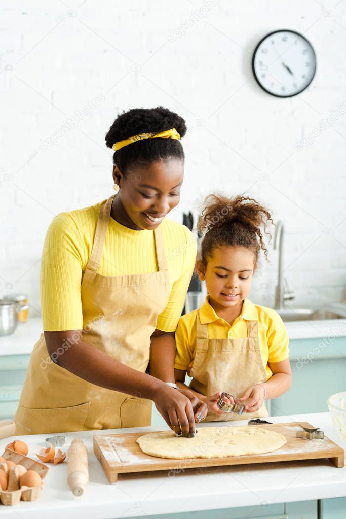 african american kid and happy mother holding cookie cutters near raw dough 