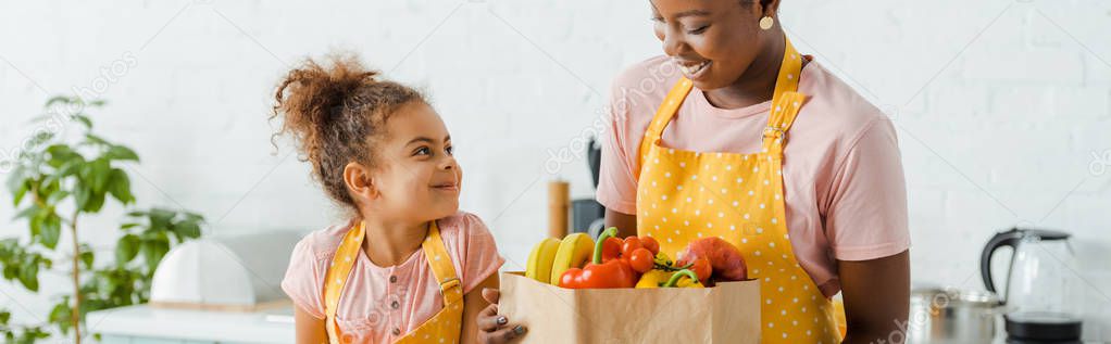 panoramic shot of happy african american kid looking at mother near groceries 
