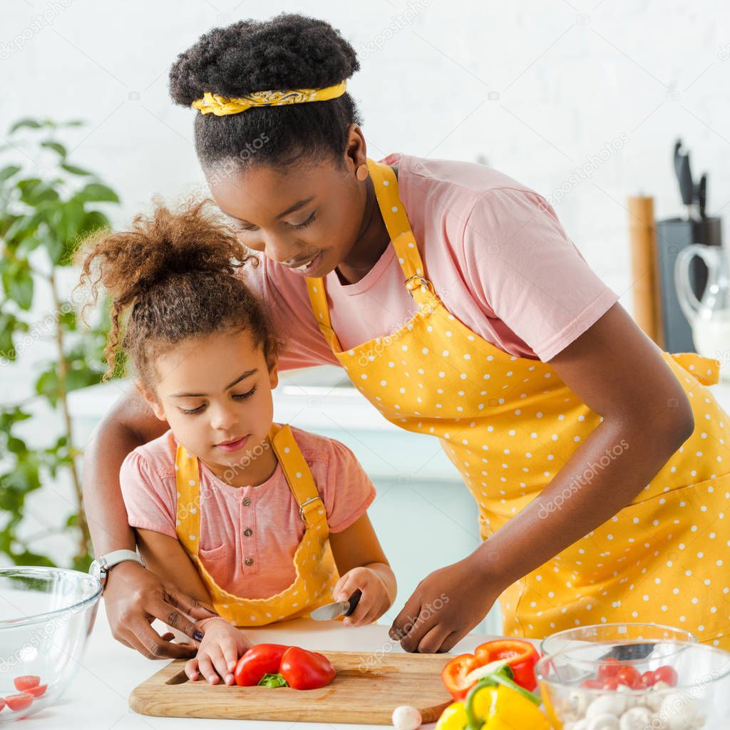 happy african american mother cutting bell pepper with cute daughter 