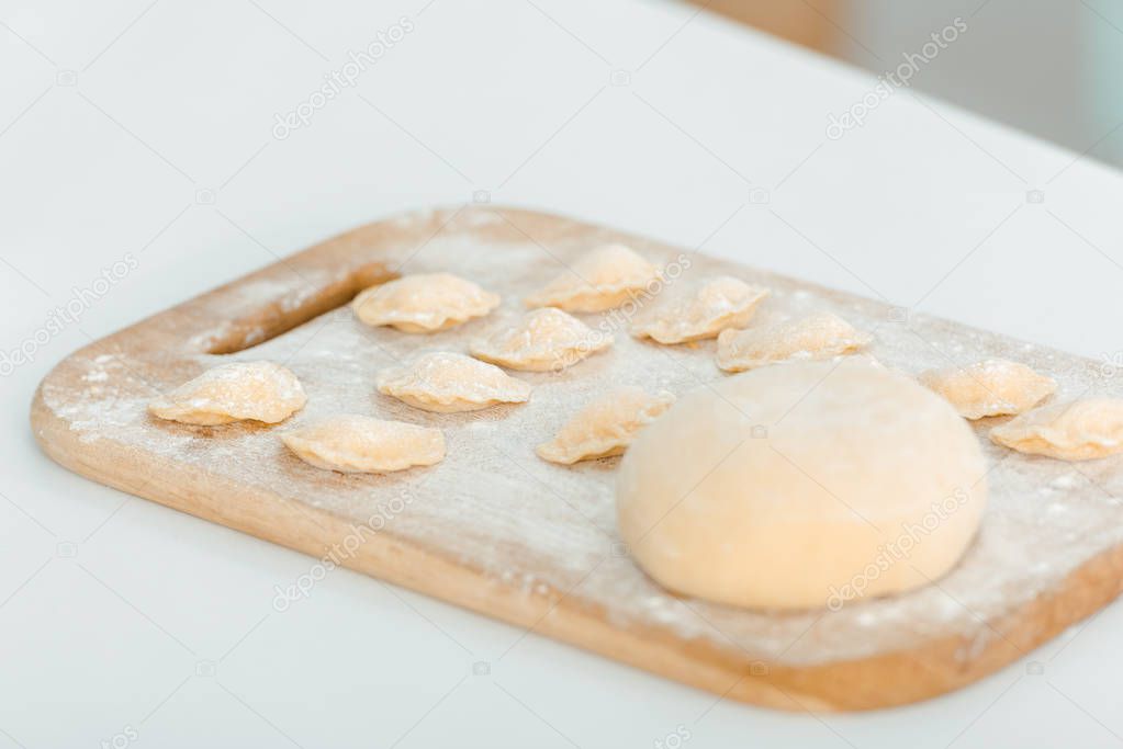 selective focus of flour near raw dumplings on wooden chopping board 