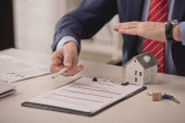 oříznutý pohled na agenta držícího ruku nad papírovým modelem domu a schránku s nápisem pojištění