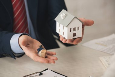 cropped view of realtor holding keys and carton house model in office  clipart
