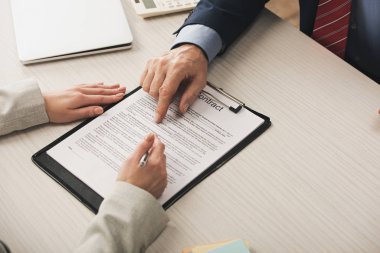 Emlakçının panoya parmağıyla işaret ettiği kırpılmış görünüm ve müşterinin yanındaki sözleşme harfleri 