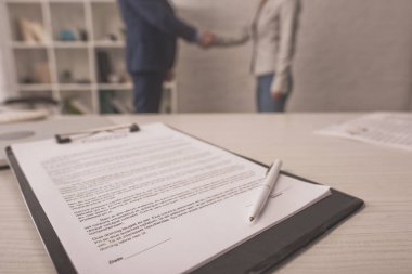 Menajer ve istemcinin el sıkışırken yanında belge olan panonun seçici odağı