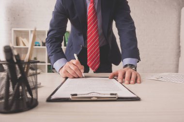 selective focus of broker signing document near stationery on desk  clipart