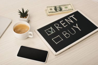 Kiralı karatahta ve kahve, bitki, boş ekran ve para ile akıllı telefon yanına harf satın 