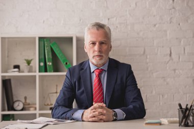Yakışıklı emlakçı sıkıca otururken kameraya bakıyor. 