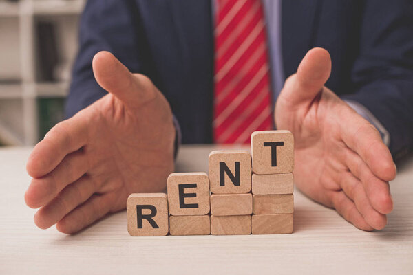 cropped view of agent putting hands on desk near wooden cubes with rent lettering 
