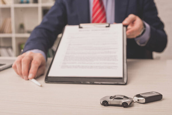 selective focus of car key near agent holding clipboard 