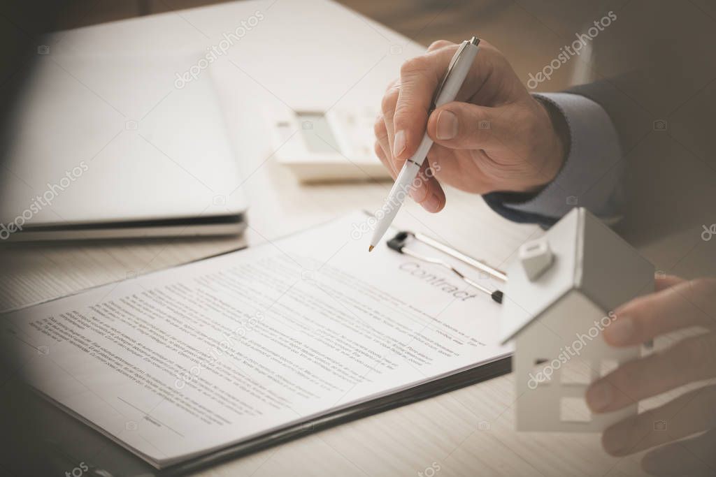 cropped view of agent holding pen and touching house model near clipboard with contract lettering 